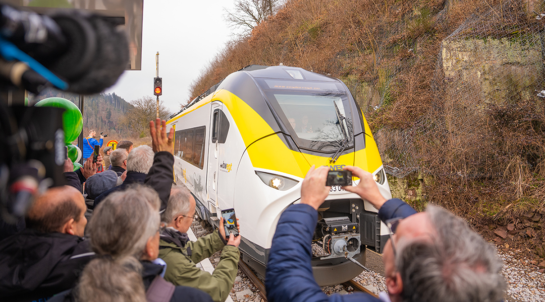 Ein Zug fährt an einem Bahnsteig ein, auf dem viele Menschen stehen.
