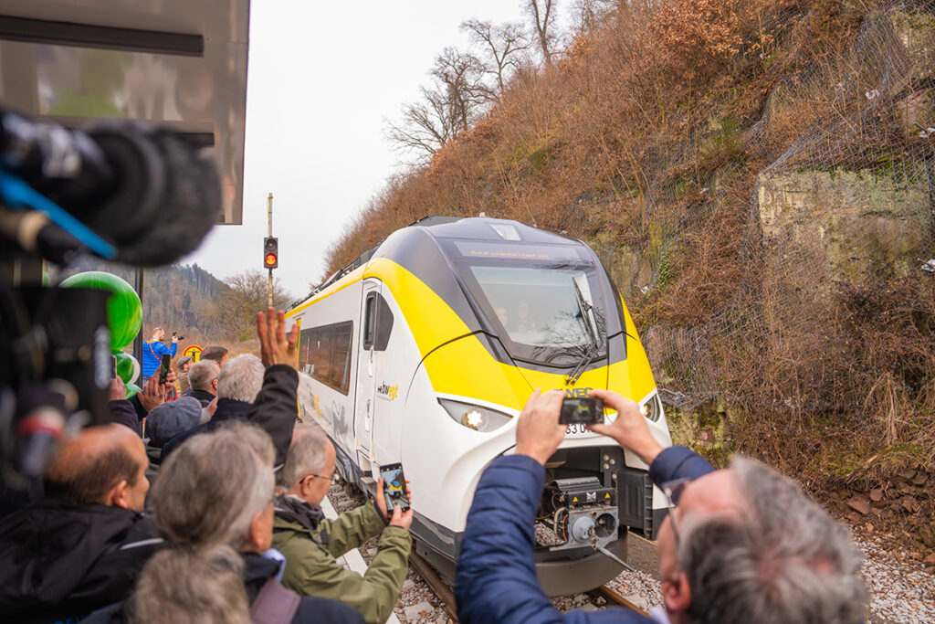 Ein Zug fährt an einem Bahnsteig ein, auf dem viele Menschen stehen.