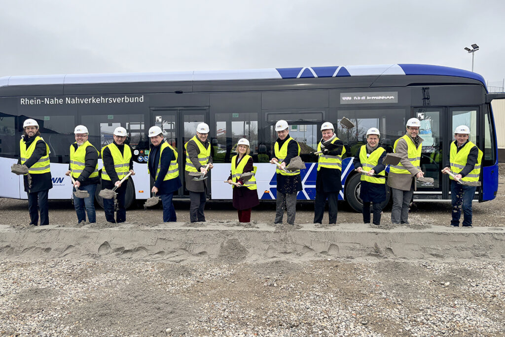 Mehrere Menschen stehen mit Schaufeln in den Händen vor einem Bus.