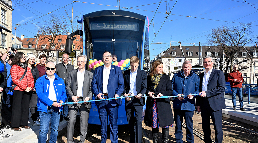 Mehrere Personen stehen vor einer Straßenbahn und schneiden ein Band durch.