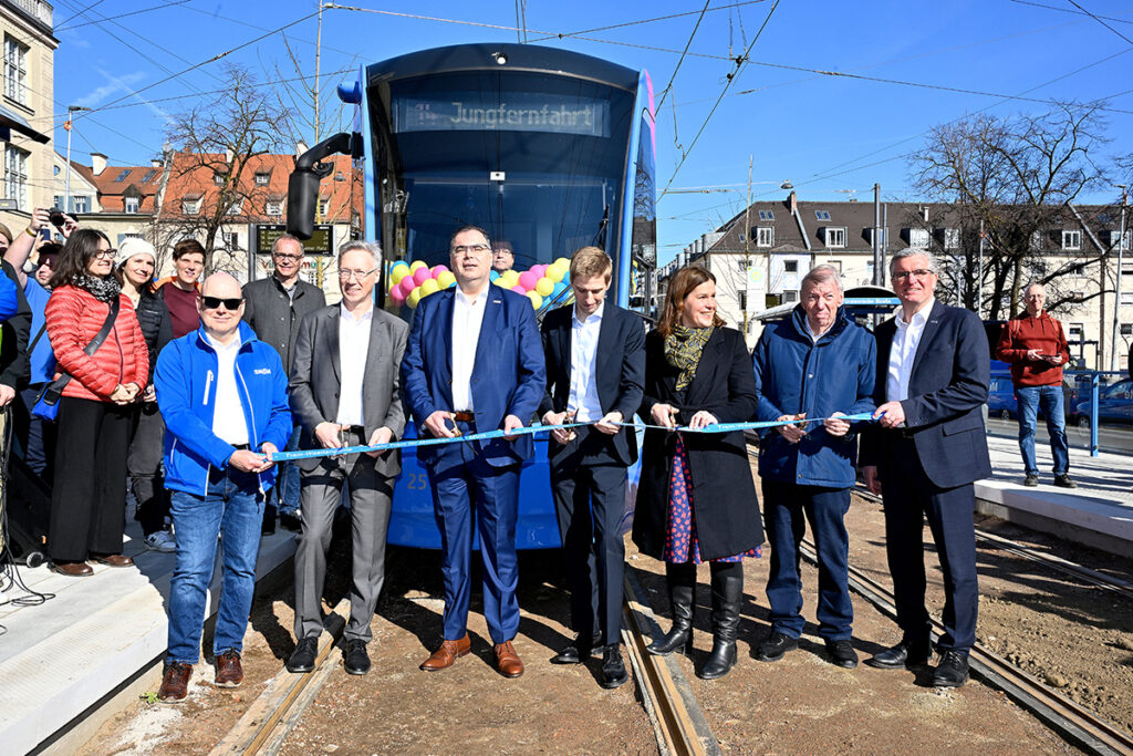 Mehrere Personen stehen vor einer Straßenbahn und schneiden ein Band durch. 