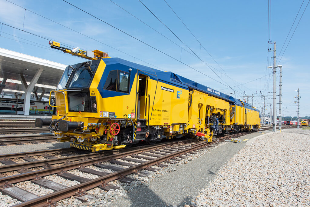 Eine Gleisbaumaschine steht in einem Bahnhof.
