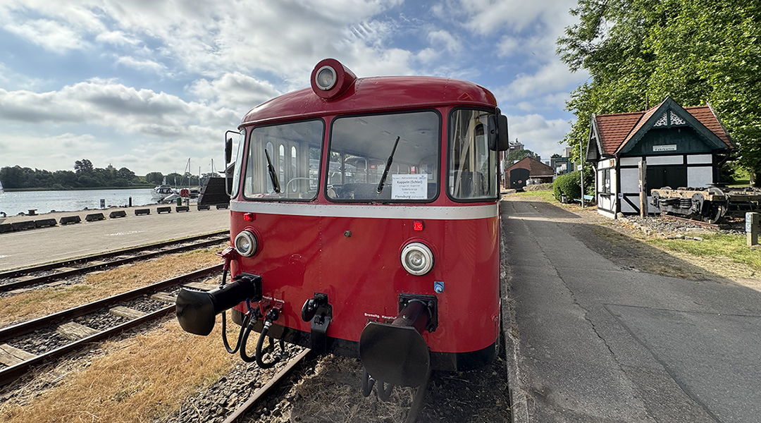 Ein Triebwagen steht an einem Bahnsteig in einem Hafengebiet.