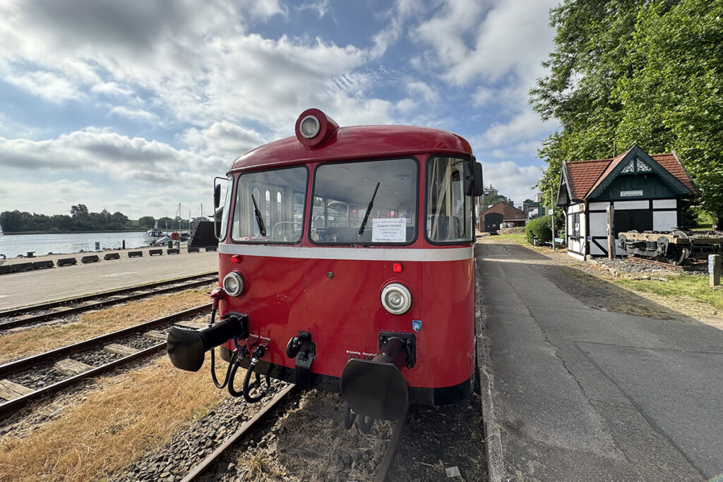 Ein Triebwagen steht an einem Bahnsteig in einem Hafengebiet.