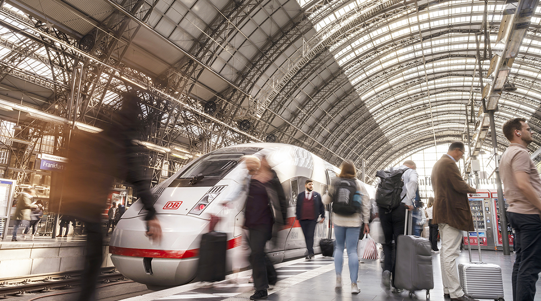 Ein ICE hält an einem Bahnsteig in einer Bahnhofshalle, auf dem Bahnsteig stehen Reisende.
