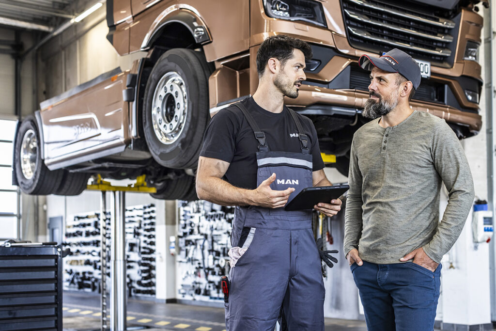 Zwei Personen stehen vor einem angehobenen LKW: