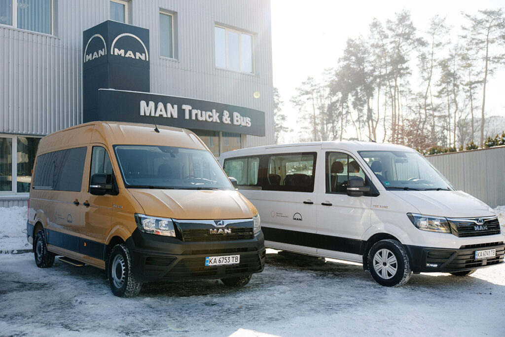 Zwei Kleinbusse stehen vor einem MAN-Firmengebäude.