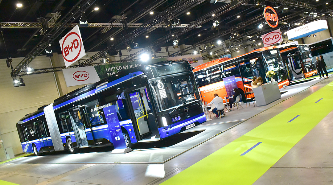 Drei Busse stehen nebeneinander in einer Messehalle.