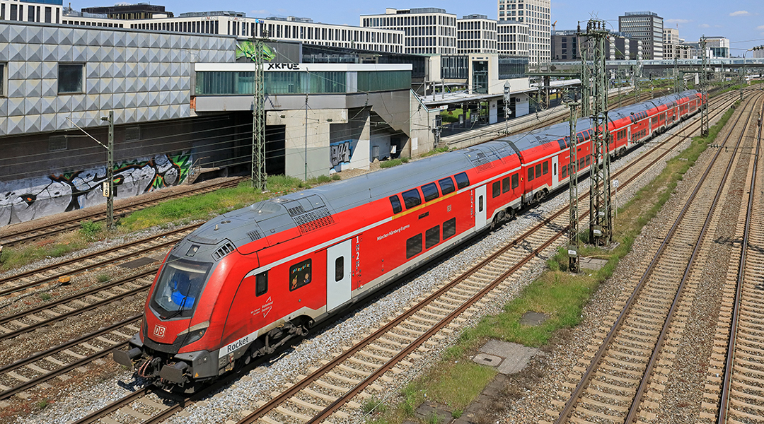 Ein Doppelstockzug fährt vor Häusern entlang.