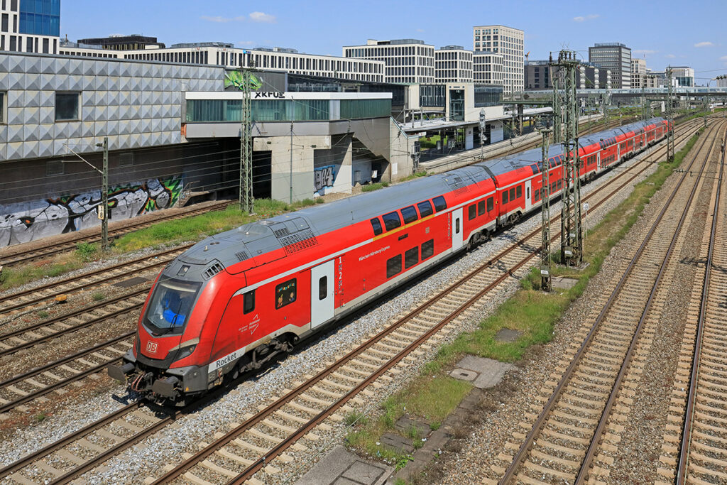 Ein Doppelstockzug fährt vor Häusern entlang.