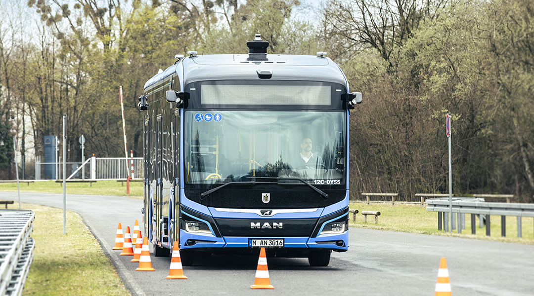 Ein automatisierter Bus fährt auf einer Straße an Leitkegeln entlang.