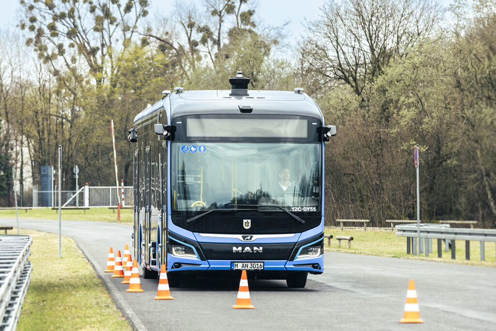 Ein automatisierter Bus fährt auf einer Straße an Leitkegeln entlang.