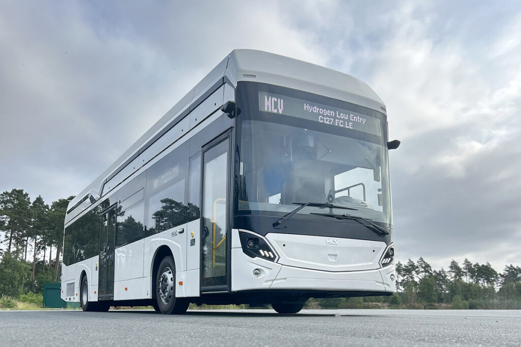 Ein Bus steht auf einem Platz vor Bäumen.