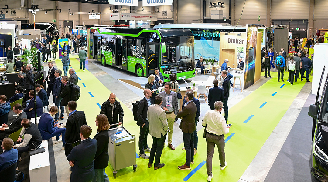 Zahlreiche Personen in einer Messehalle mit Bussen.