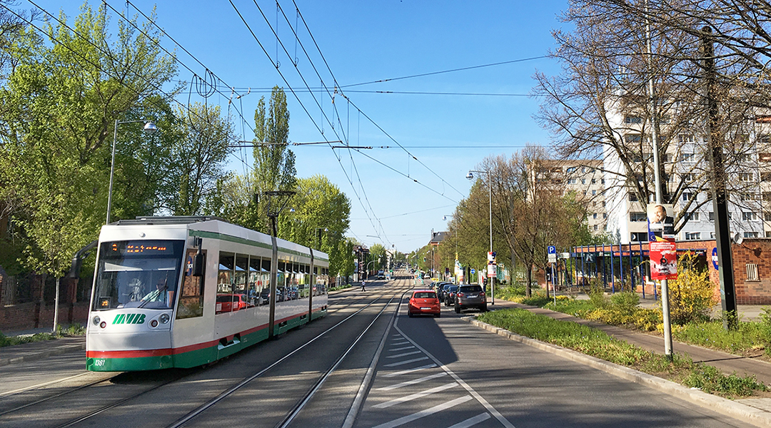 Eine Straßenbahn fährt auf einer breiten Straße vor Häusern.
