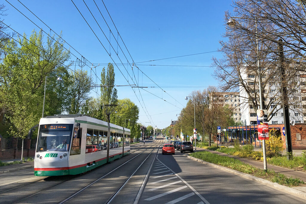 Eine Straßenbahn fährt auf einer breiten Straße vor Häusern.