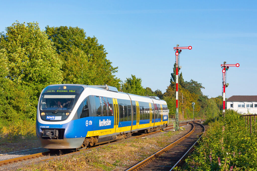 Ein Triebzug fährt vor Signalen und Bäumen auf einem Gleis.