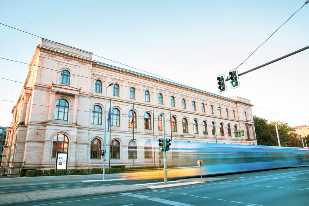 Eine Straßenbahn fährt vor einem großen Gebäude entlang.