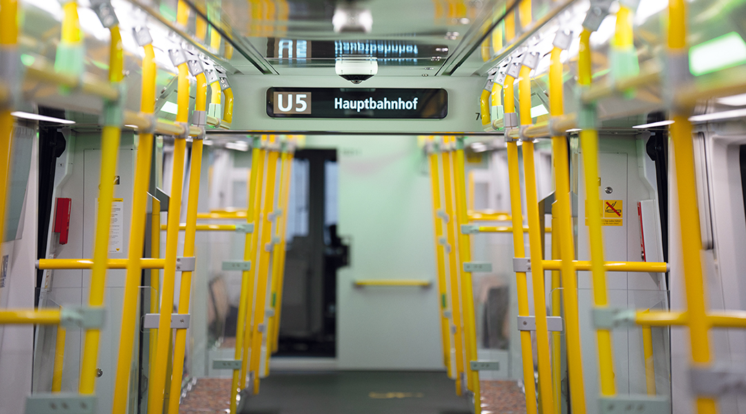 Innenraum einer neuen Berliner U-Bahn mit Infoanzeige und Haltestangen.