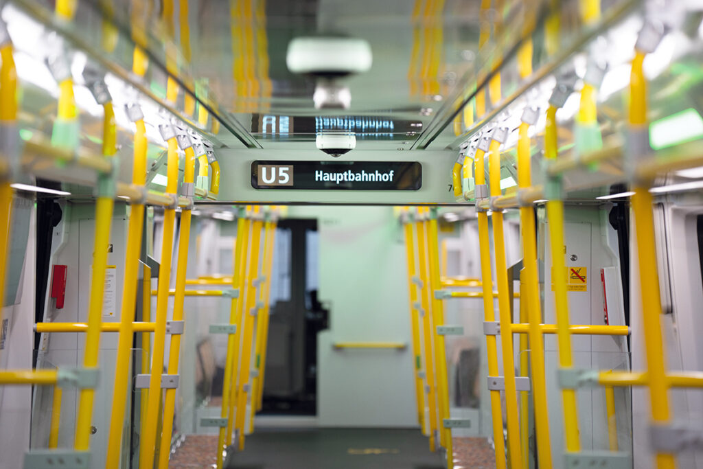 Innenraum einer neuen Berliner U-Bahn mit Infoanzeige und Haltestangen.