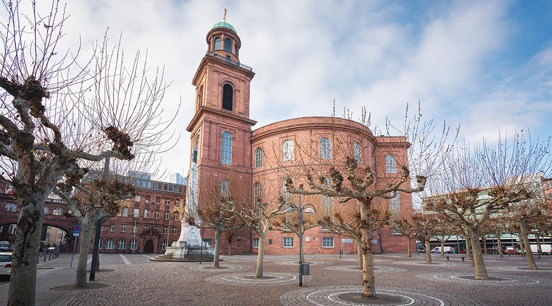 Über einem Platz mit niedrigen Bäumen erhebt sich die Paulskirche.