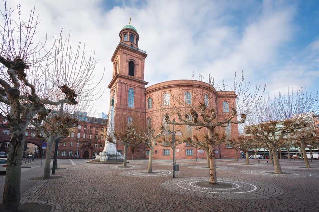 Über einem Platz mit niedrigen Bäumen erhebt sich die Paulskirche.