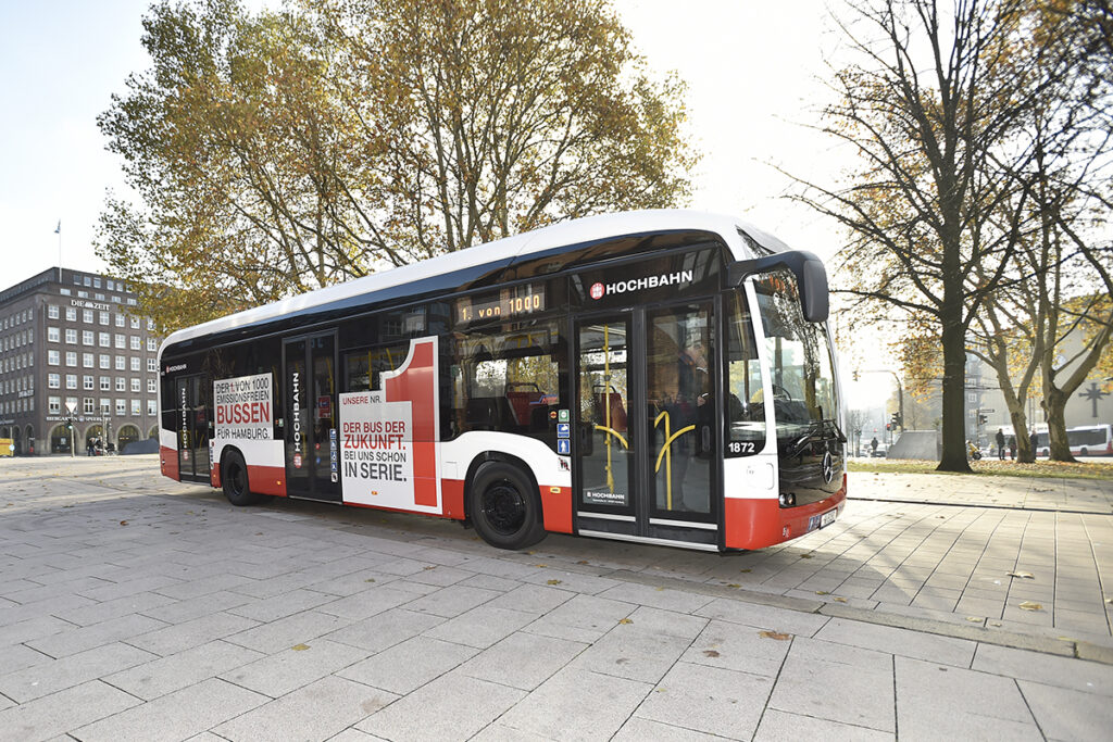 Ein Elektrobus steht unter Bäumen auf einer Straße.