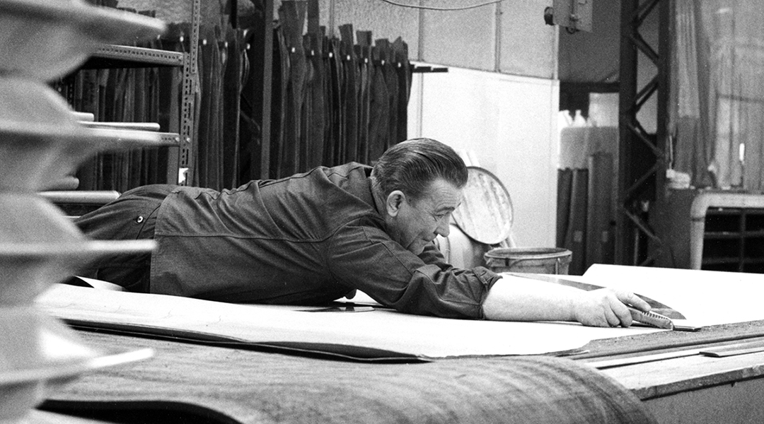 Historisches Bild einer Person, die Stoffe auf einem Tisch mit einem Messer schneidet.