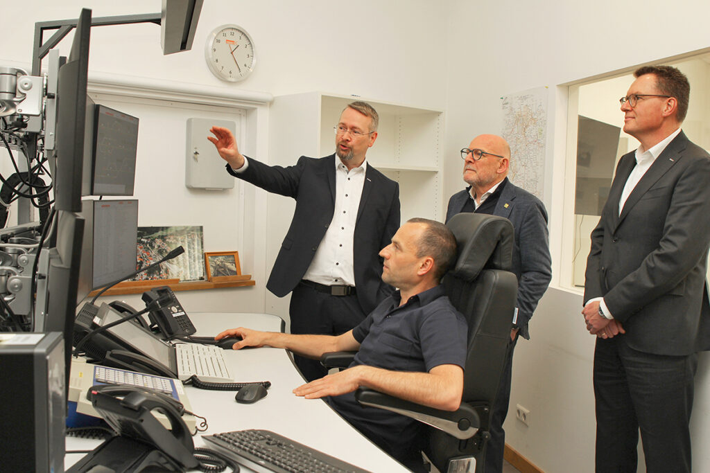 Mehrere Personen stehen in einem Raum und schauen auf Monitore.