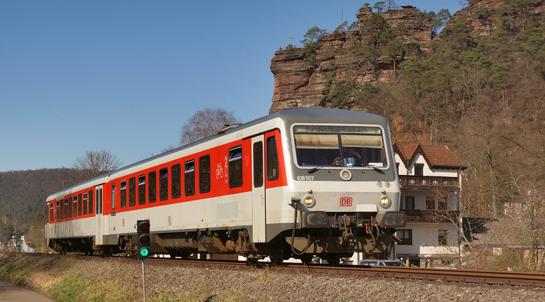 Ein Triebwagen fährt vor einer Felswand entlang.