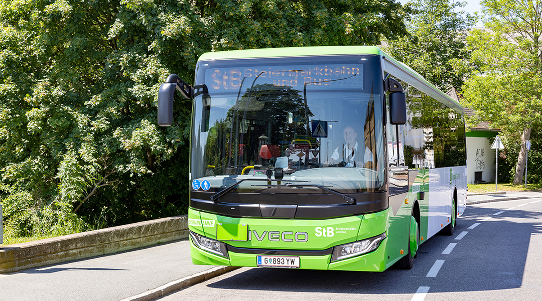 Ein Überlandbus fährt auf einer Straße unter Bäumen.