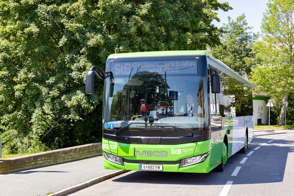 Ein Überlandbus fährt auf einer Straße unter Bäumen.