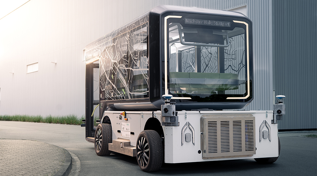 Ein autonomes Shuttle mit einer Personenkabine steht vor einer Halle.