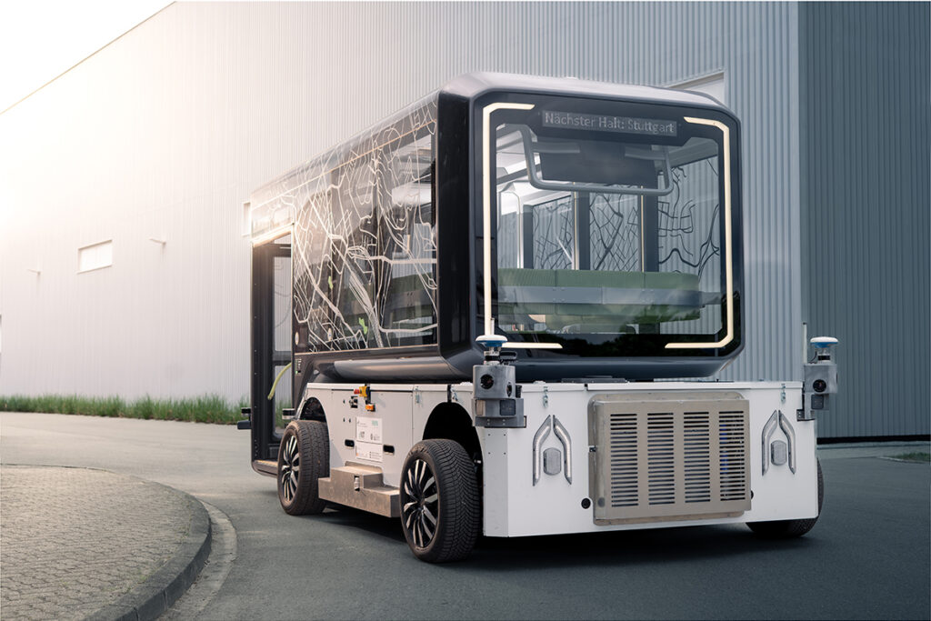 Ein autonomes Shuttle mit einer Personenkabine steht vor einer Halle.