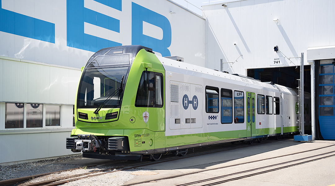 Ein Triebzug steht auf einem Gleis vor einer Halle.
