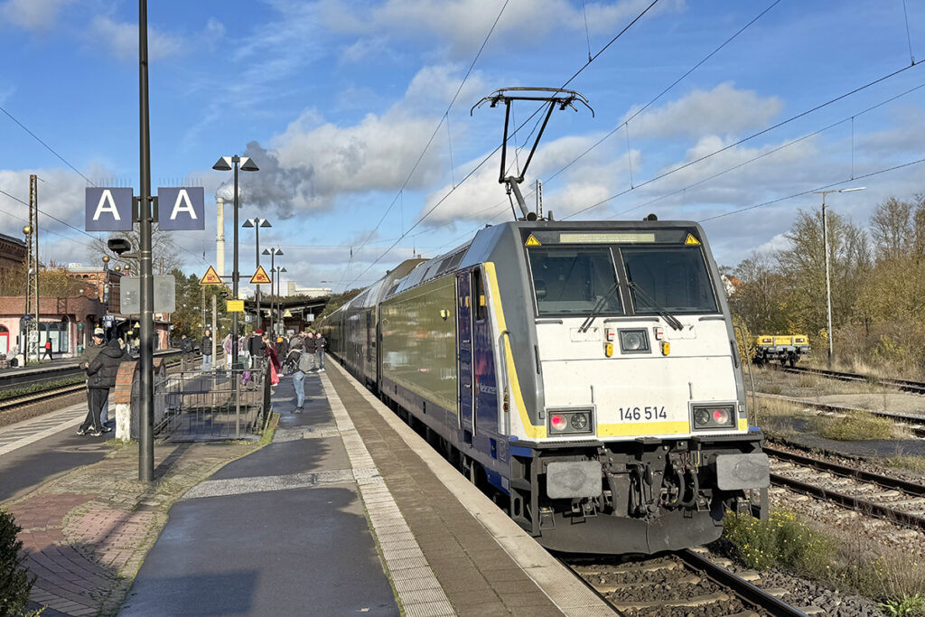 Ein Zug mit einer Elektrolok hält an einem Bahnsteig.