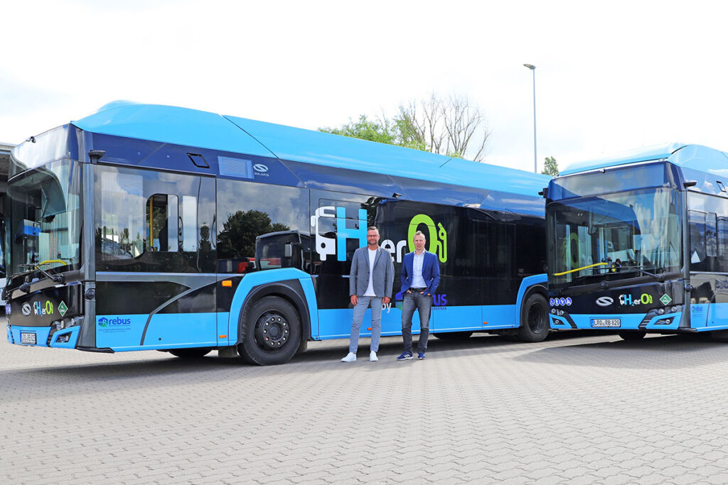 Zwei Personen stehen vor zwei Wasserstoffbussen.