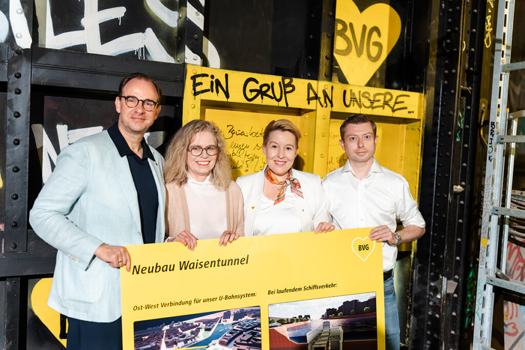 Vier Personen steht hinter einem Schild vor einer Tunnelwand.