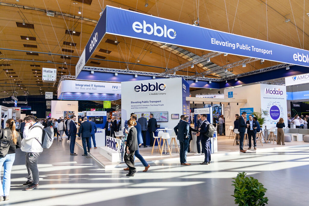 Ein Messestand mit vielen Leuten in einer Halle.