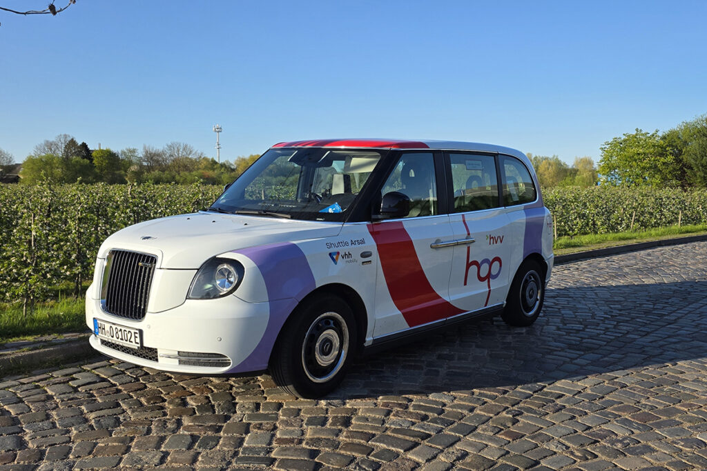 Ein On-Demand-Fahrzeug steht vor Bäumen auf einer Straße.
