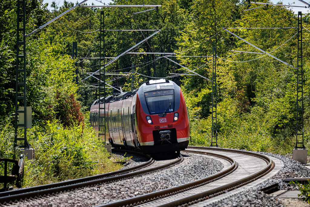 Ein Zug fährt auf einer zweigleisigen Strecke durch einen Wald.