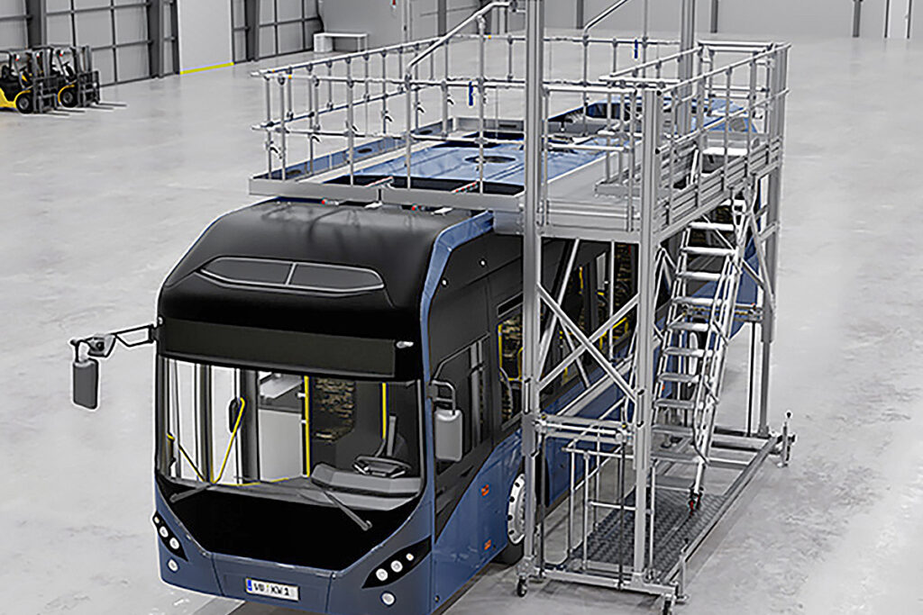 Ein Bus steht neben einer Arbeitsbühne in einer Halle.