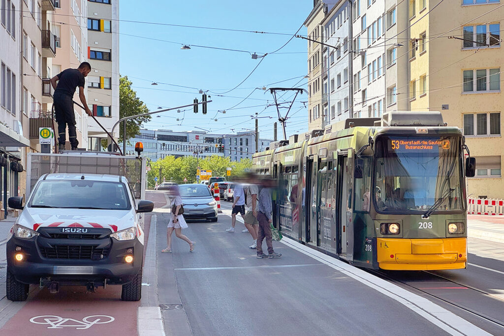 Eine Straßenbahn hält an einer Haltestelle, Personen steigen ein und aus.