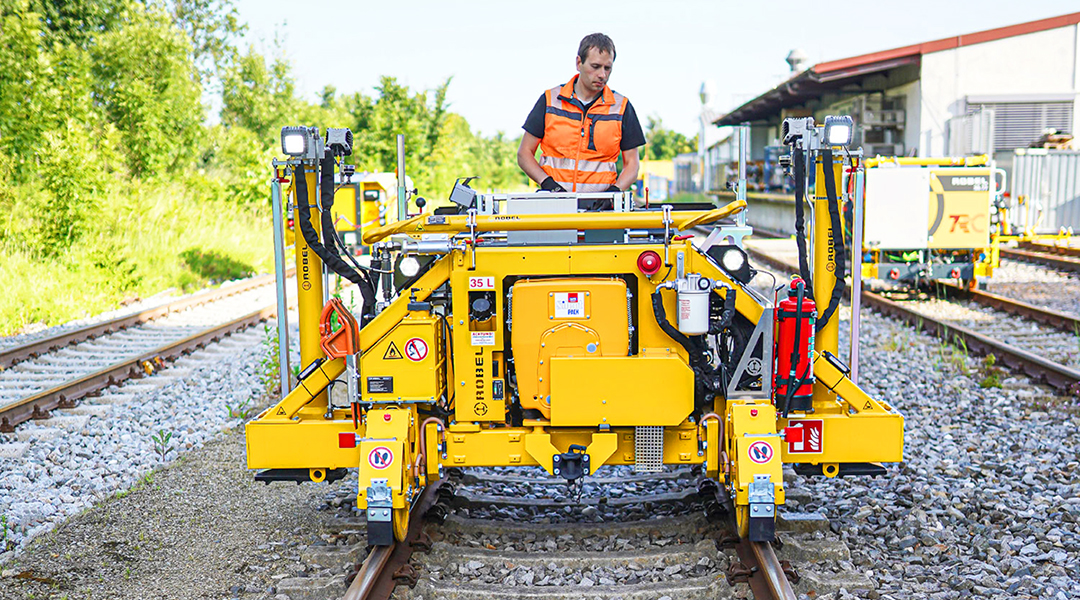 Eine Person steht auf einer kleinen Gleisbaumaschine auf einem Gleis.
