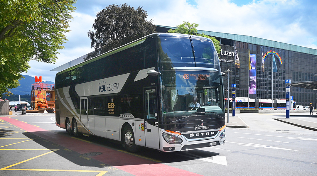 Ein Doppelstockbus fährt vor einer Bahnhofshalle im Hintergrund.