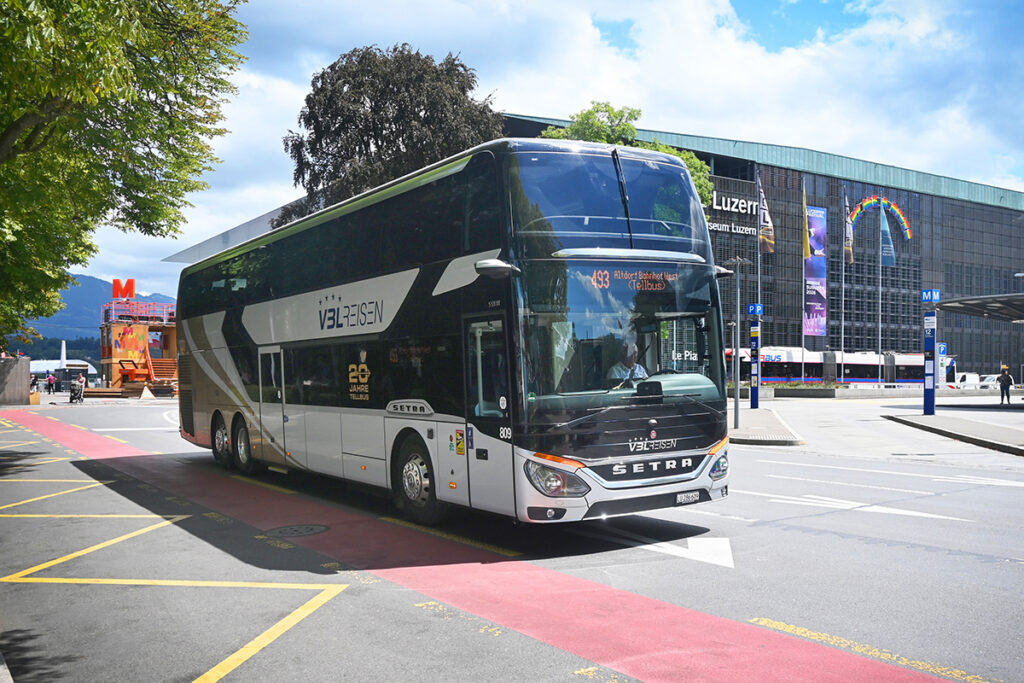 Ein Doppelstockbus fährt vor einer Bahnhofshalle im Hintergrund.