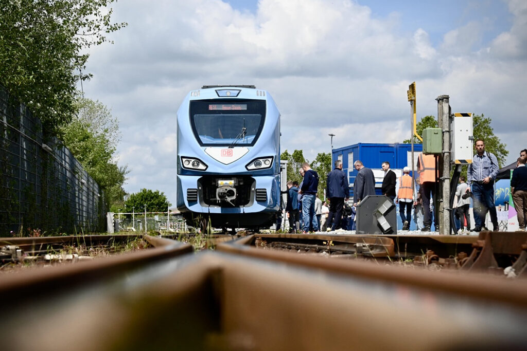 Ein Zug steht auf einem Gleis, daben stehen mehrere Personen.