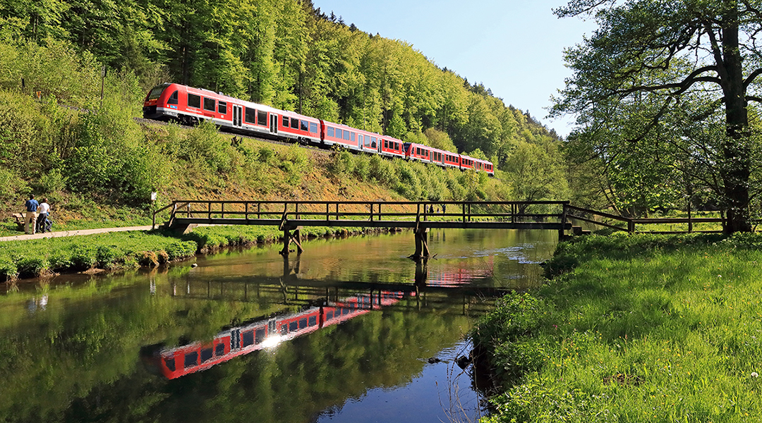 Ein Zug fährt an einem Fluss entlang und spiegelt sich im Wasser.
