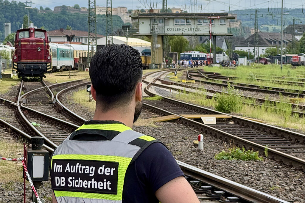 Eine Person steht vor Gleisen mit einer Lokomotive.