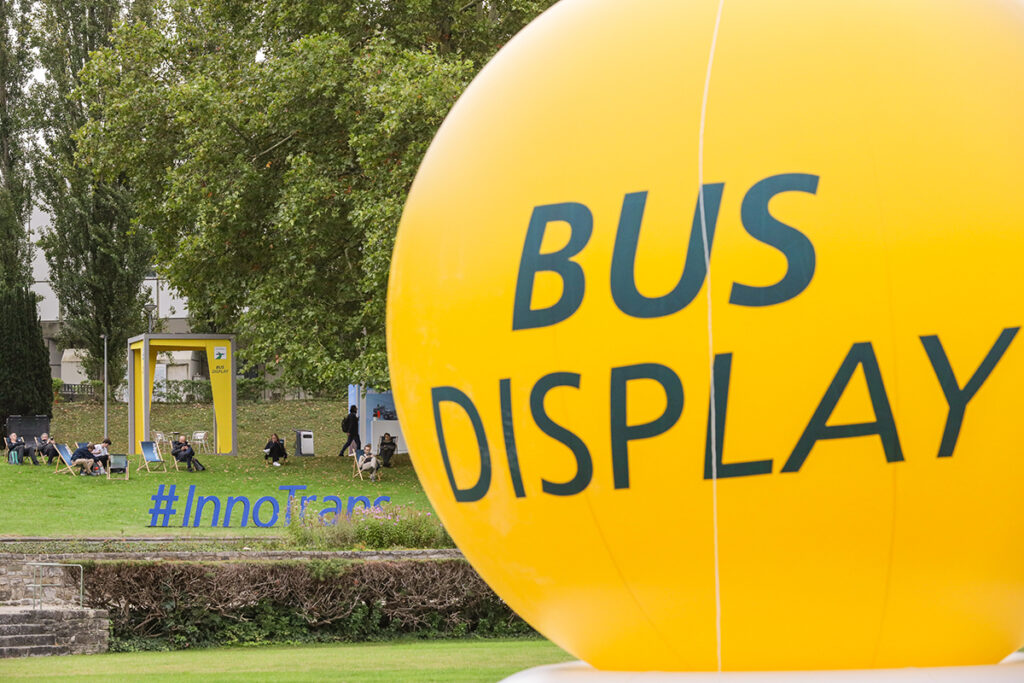 Ein Ballon mit der Aufschrift Bus Display schwebt vor einer Grünanlage.